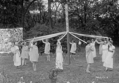 Women standing in a circle twirling ribbons around a May pole